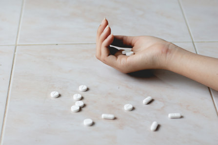 Teenager’s hand on a floor with pills.