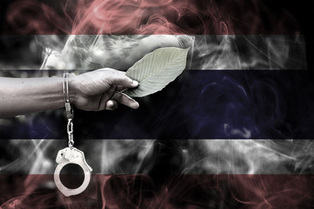 Hand holding kratom in handcuffs in front of the Thailand flag.