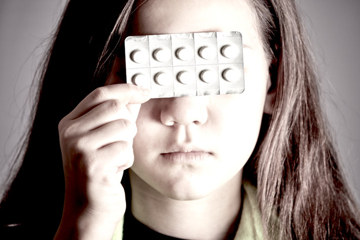 Girl holding pills in front of her face.