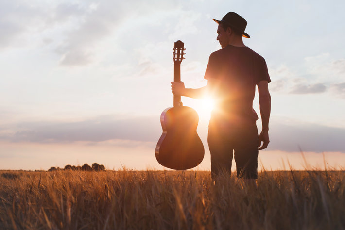 Man is standing with a guitar in a sunshine