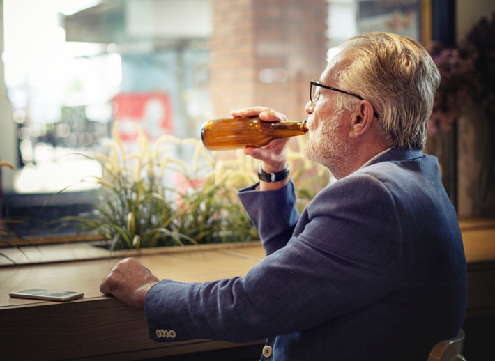 An old man is drinking alcohol.