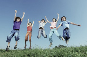 Group of five happy children jumping outdoors.